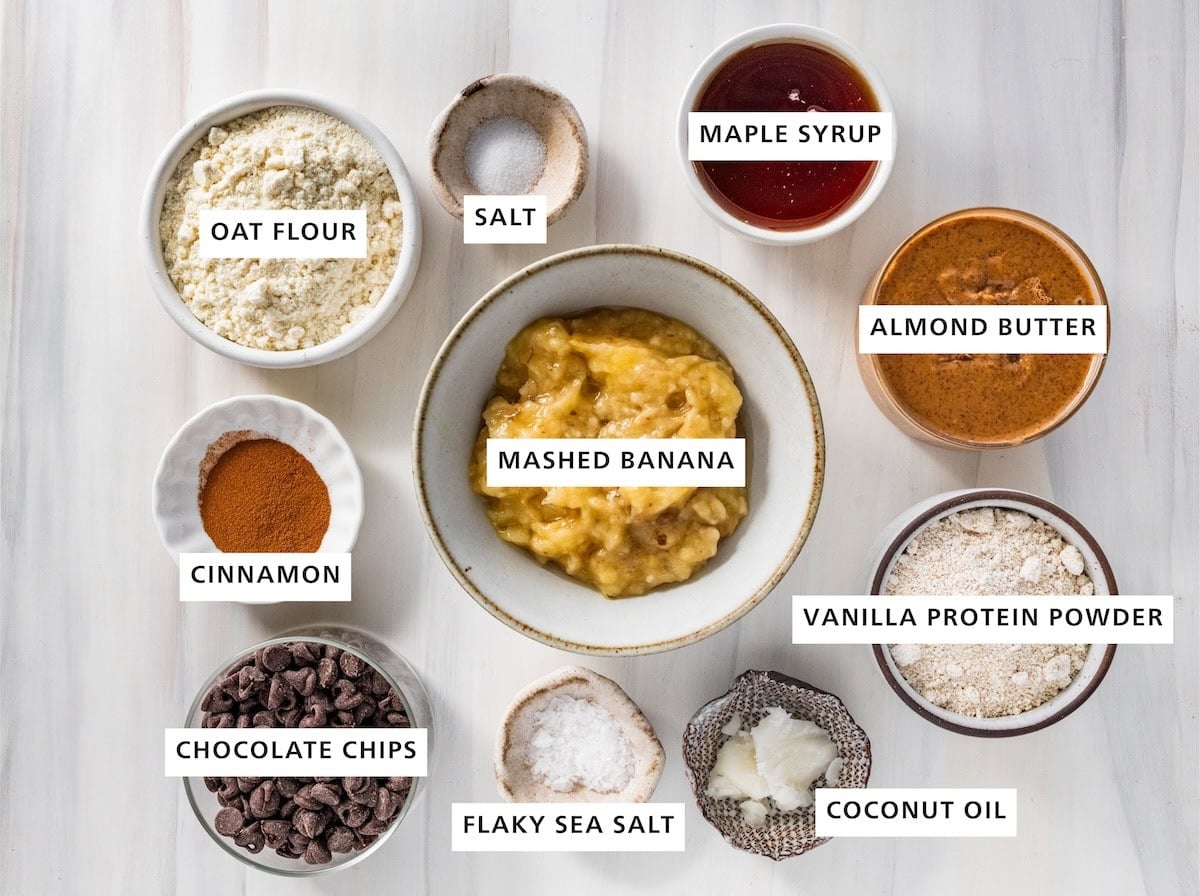 Ingredients for banana bread protein balls: mashed banana, oat flour, salt, maple syrup, almond butter, vanilla protein powder, coconut oil, sea salt, chocolate chips and cinnamon.