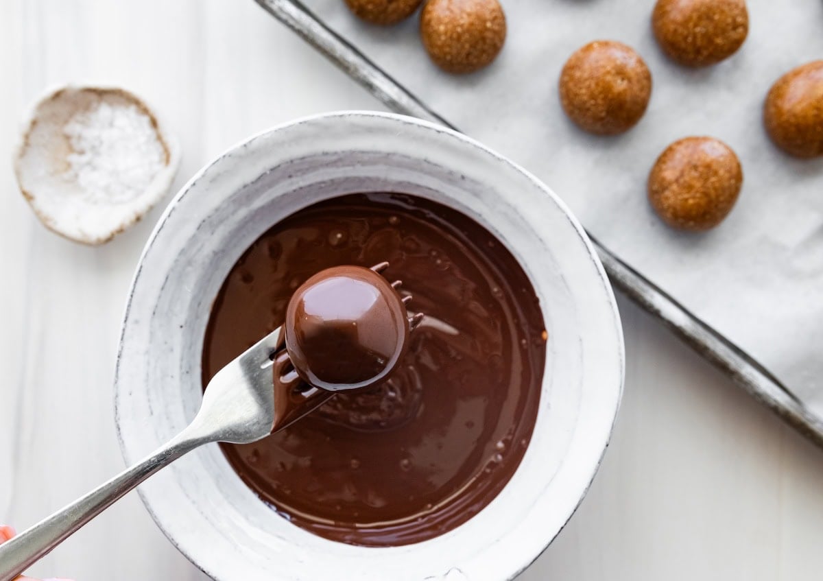 A fork scooping a banana bread protein ball out of a bowl of melted chocolate.