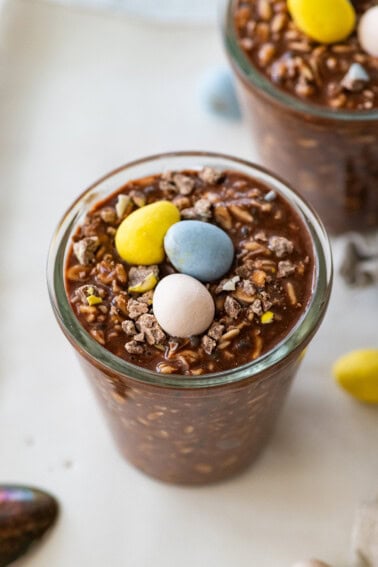 2 Cadbury mini egg overnight oats in glass jars each topped with 3 Cadbury eggs.