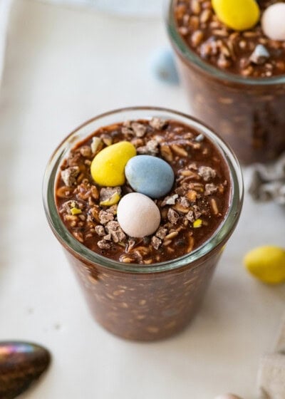 2 Cadbury mini egg overnight oats in glass jars each topped with 3 Cadbury eggs.
