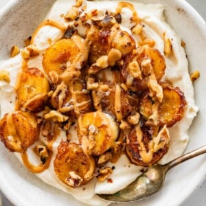 A caramelized banana yogurt bowl in a speckled bowl topped with a drizzle of peanut butter and chopped walnuts.