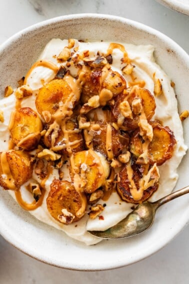 A caramelized banana yogurt bowl in a speckled bowl topped with a drizzle of peanut butter and chopped walnuts.
