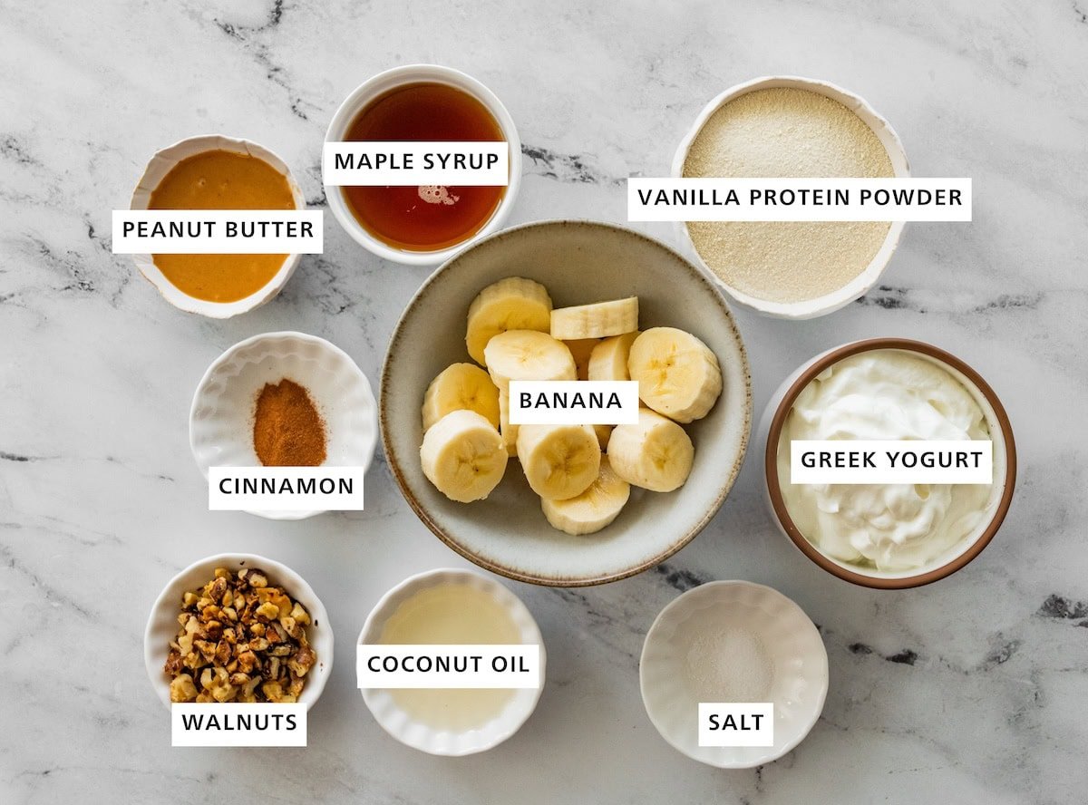 Ingredients measured out for a caramelized banana yogurt bowl: peanut butter, maple syrup, vanilla protein powder, bananas, cinnamon, greek yogurt, salt, coconut oil, walnuts, and cinnamon.