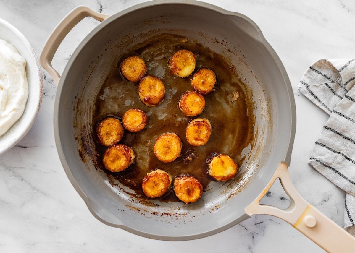 Banana slices being caramelized in a pan with maple syrup and cinnamon.