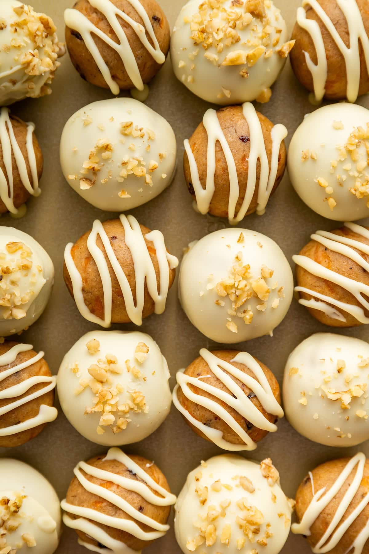 Carrot cake protein balls with white chocolate drizzle and crushed walnuts on top.
