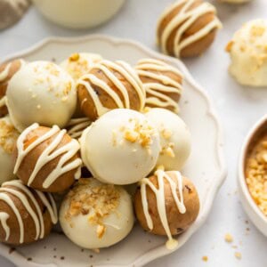 White chocolate covered carrot cake protein balls topped with crushed walnuts on a serving plate.