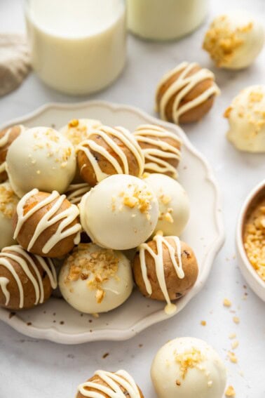 White chocolate covered carrot cake protein balls topped with crushed walnuts on a serving plate.