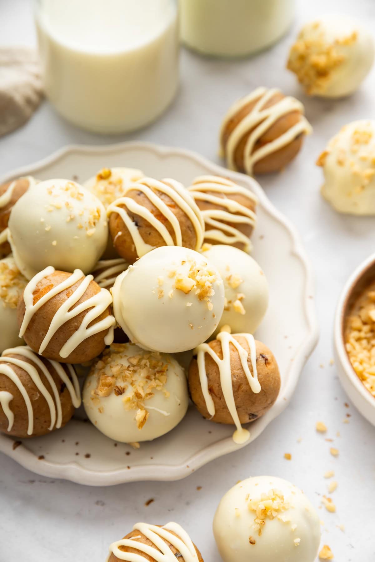 White chocolate covered carrot cake protein balls topped with crushed walnuts on a serving plate.