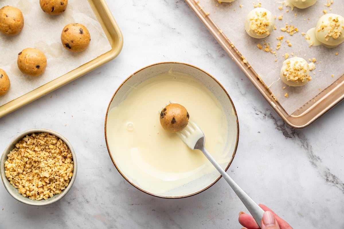 Dipping carrot cake protein ball into melted white chocolate coating with a fork in a small bowl.