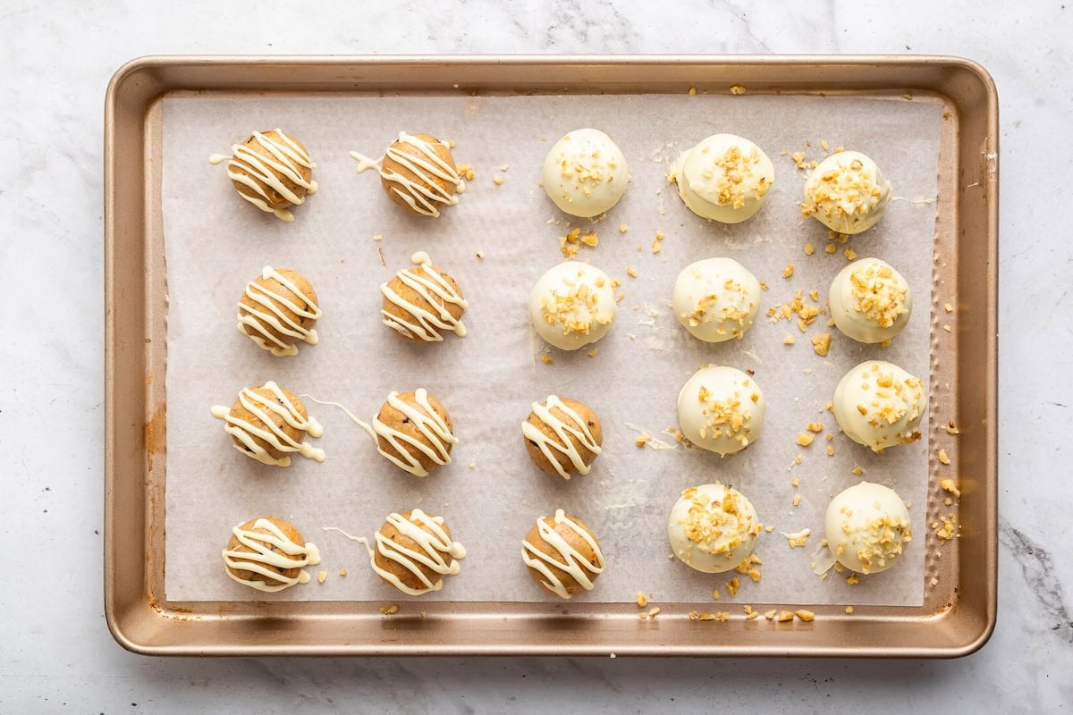 Carrot cake protein balls dipped in white chocolate on a tray with drizzle and crushed walnuts.
