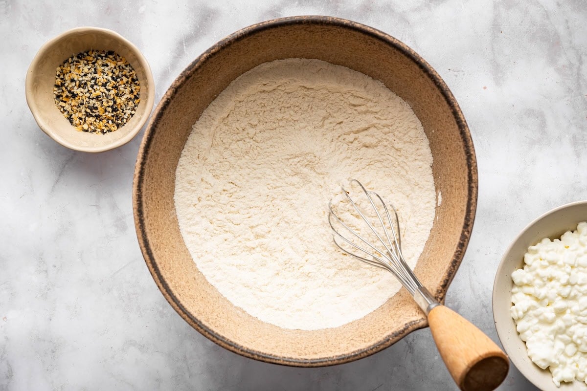 Flour and baking powder whisked together in bowl for bagel dough.
