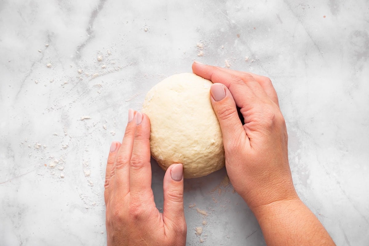 Dough ball being kneaded on surface for cottage cheese bagel recipe.