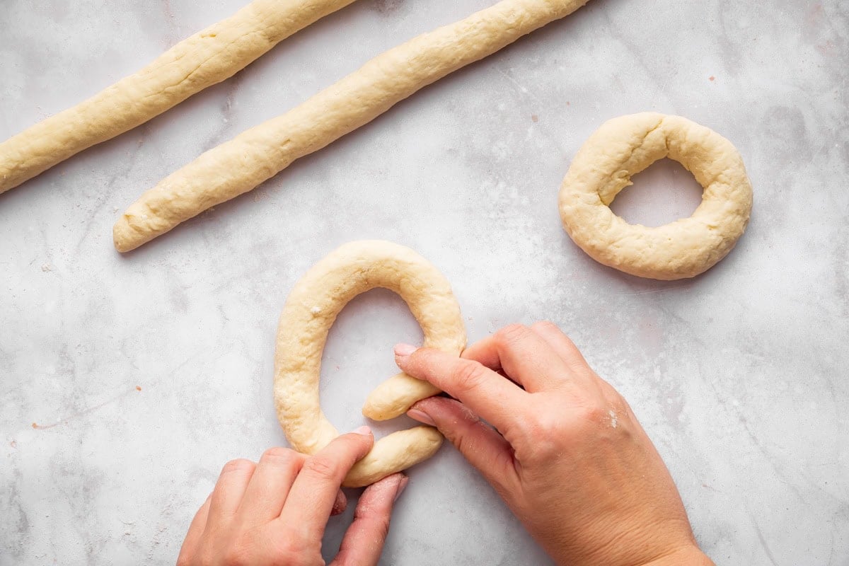 Hands rolling dough into rope to shape homemade cottage cheese bagels.