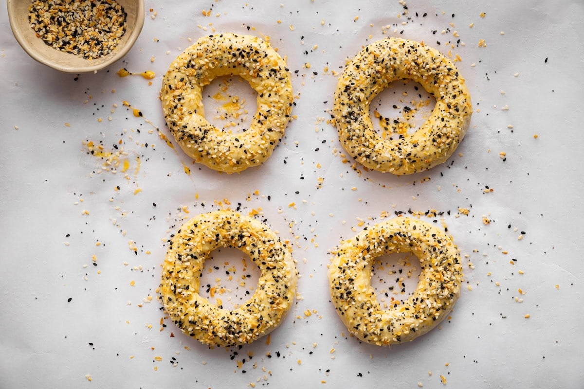 Unbaked cottage cheese bagels on baking sheet topped with everything bagel seasoning.
