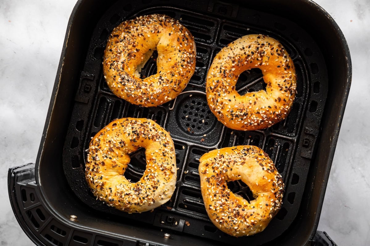 Air fryer basket filled with golden cottage cheese bagels topped with seasoning.