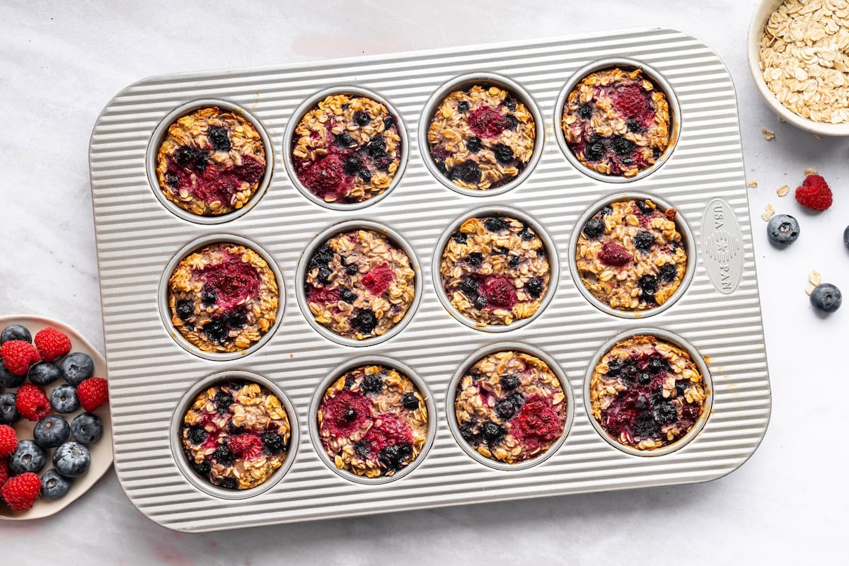 Cooked cottage cheese baked oatmeal cups with mixed berries in a muffin tin.