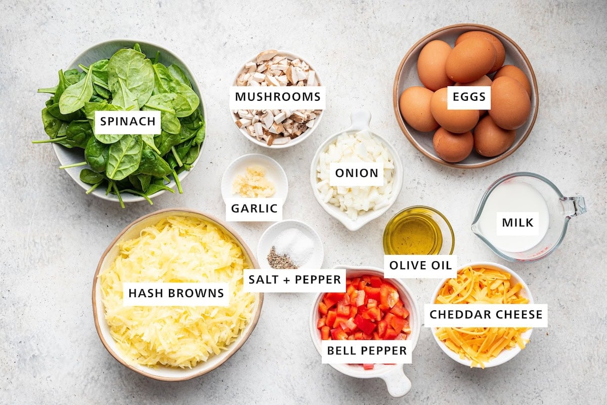 Ingredients measured out to make Vegetarian Hash Brown Breakfast Casserole: shredded frozen hash browns, baby spinach, garlic, mushrooms, salt, pepper, bell pepper, onion, olive or avocado oil, eggs, cheddar cheese and non-dairy milk.