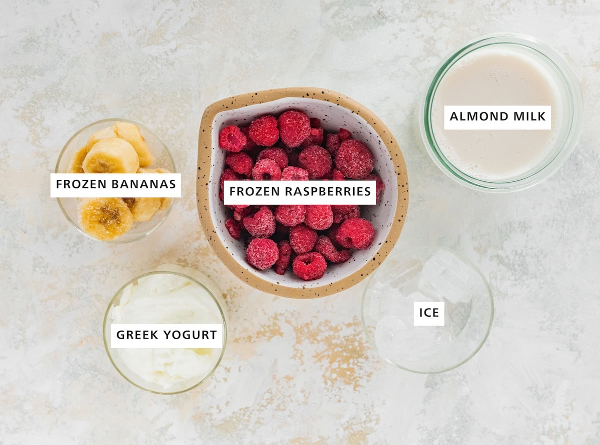 Ingredients measured out to make Raspberry Smoothie: almond milk, ice, frozen raspberries, frozen banana and Greek yogurt.