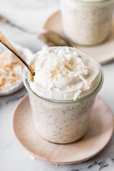 Creamy coconut overnight oats topped with whipped cream and lightly toasted shredded coconut.