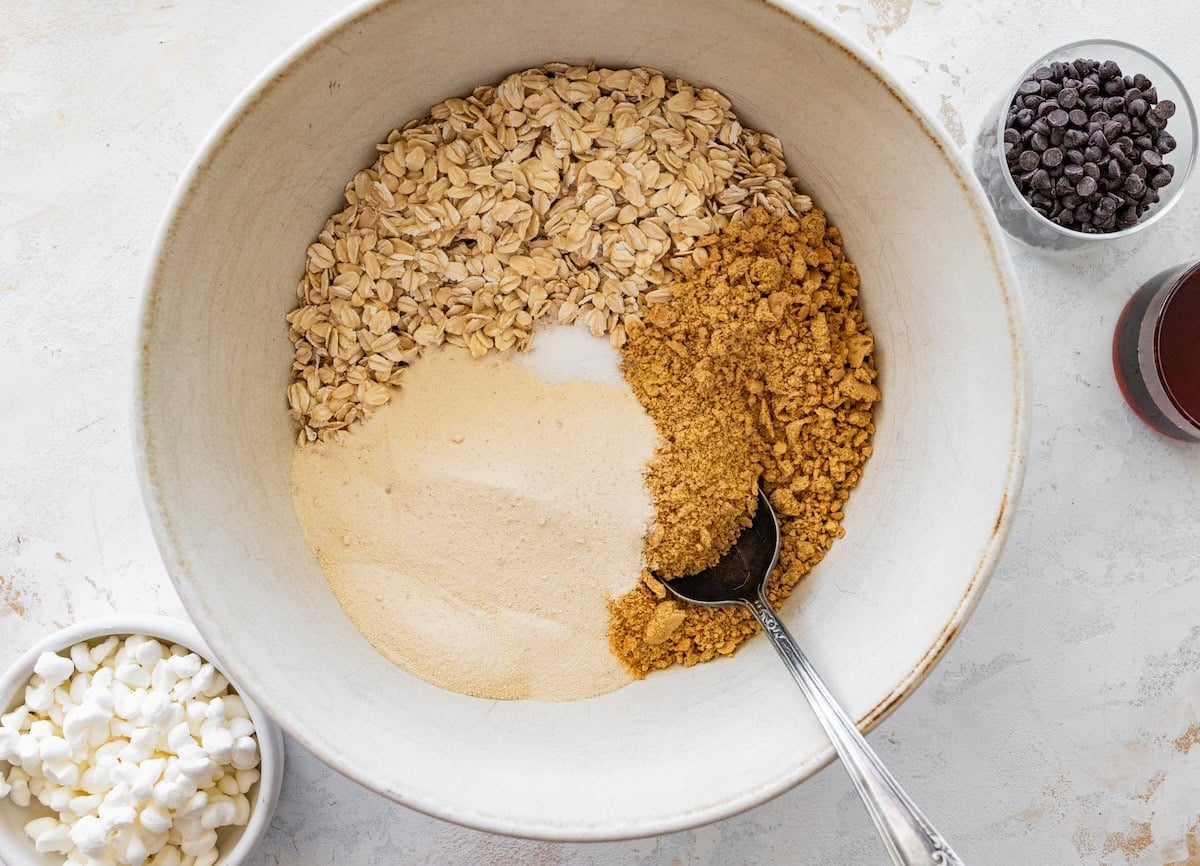 Oats, graham crackers and protein powder in a bowl for s&rsquo;mores protein balls being mixed with a spoon.