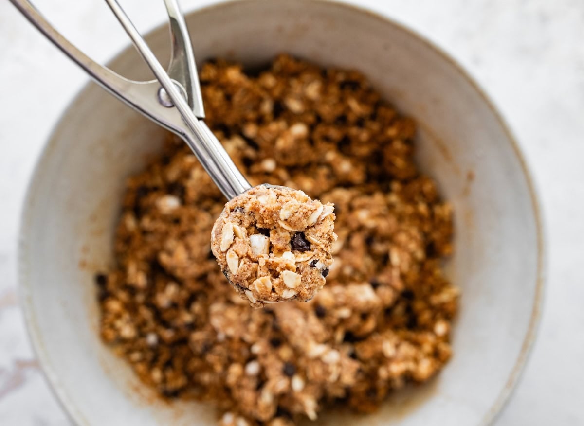Scooping s&rsquo;mores protein ball mixture with a cookie scoop from a mixing bowl.