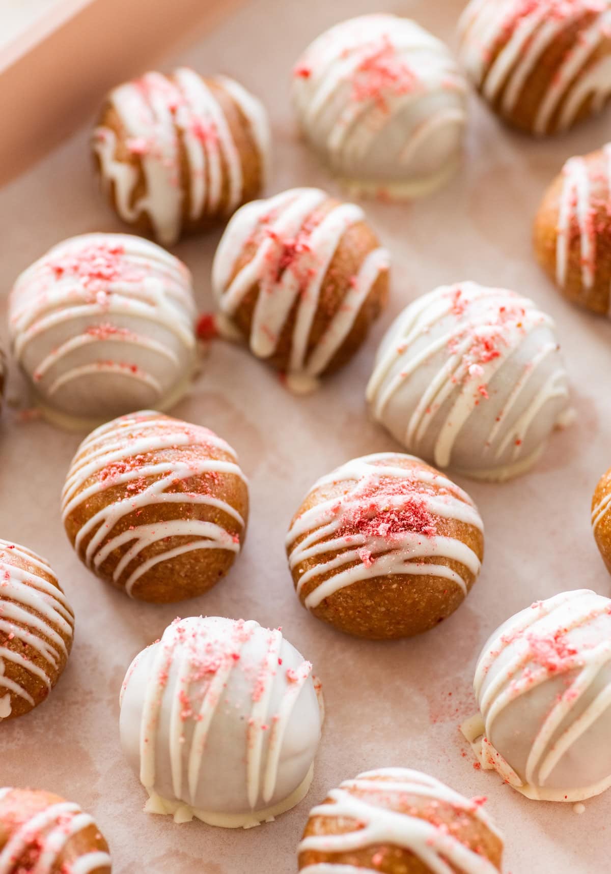 Strawberry protein balls on a parchment-lined tray with a white chocolate coating and strawberry topping.