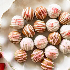 Strawberry protein balls coated in white chocolate topped with crushed freeze-dried strawberries on a serving plate.