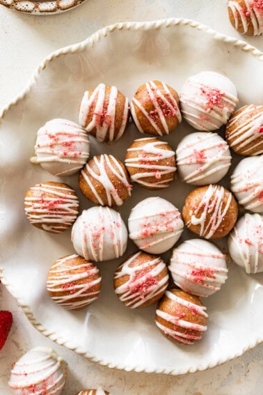 Strawberry protein balls coated in white chocolate topped with crushed freeze-dried strawberries on a serving plate.