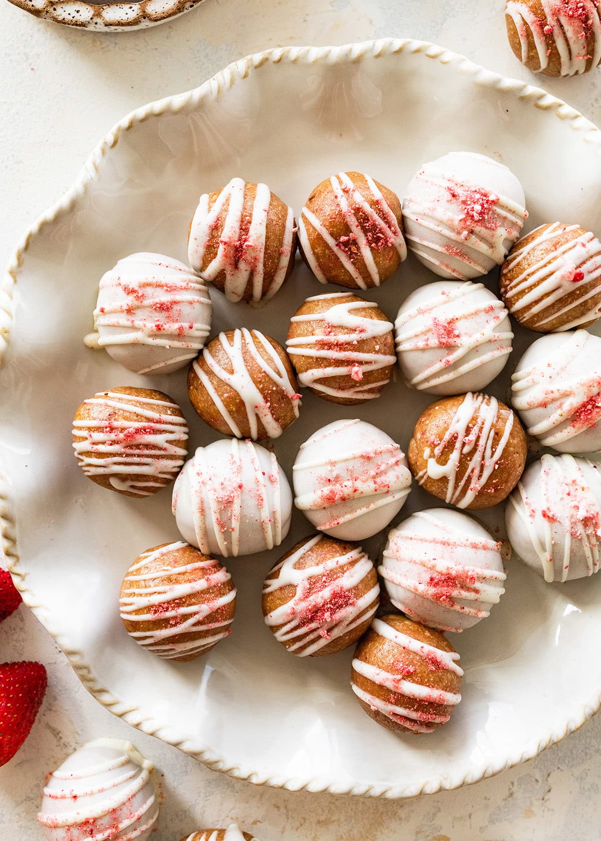 Strawberry protein balls coated in white chocolate topped with crushed freeze-dried strawberries on a serving plate.