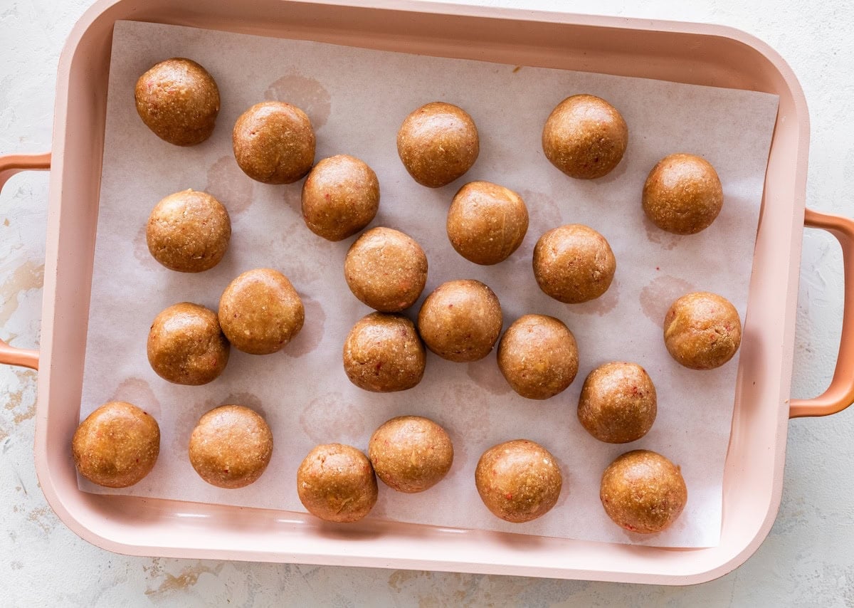 Rolled strawberry protein balls lined up on a baking sheet before coating.