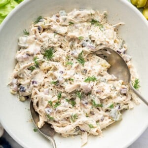 Dill pickle chicken salad in a large serving bowl with two serving spoons and topped with fresh dill.