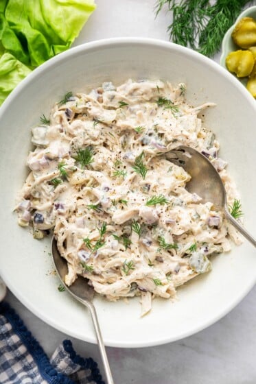 Dill pickle chicken salad in a large serving bowl with two serving spoons and topped with fresh dill.