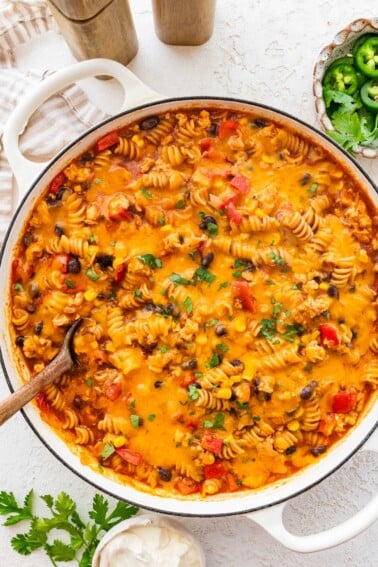 Enchilada pasta in a Dutch oven topped with melted cheese and fresh cilantro.