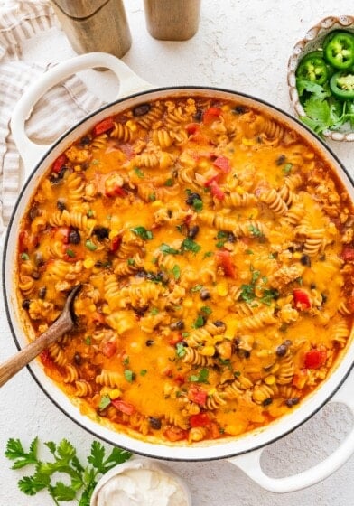 Enchilada pasta in a Dutch oven topped with melted cheese and fresh cilantro.