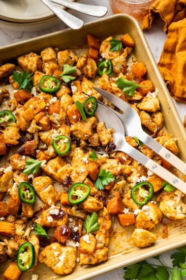 Hot honey glazed chicken on a baking sheet with roasted cauliflower, sweet potatoes, jalapeรฑo slices, feta, and cilantro.