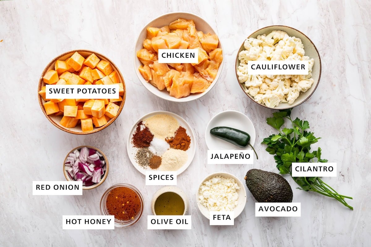 Ingredients measured in small dishes for hot honey chicken sheet pan meal: chicken, cauliflower, sweet potatoes, red onion, spices, hot honey, olive oil, feta, jalape&ntilde;o, avocado, and cilantro.