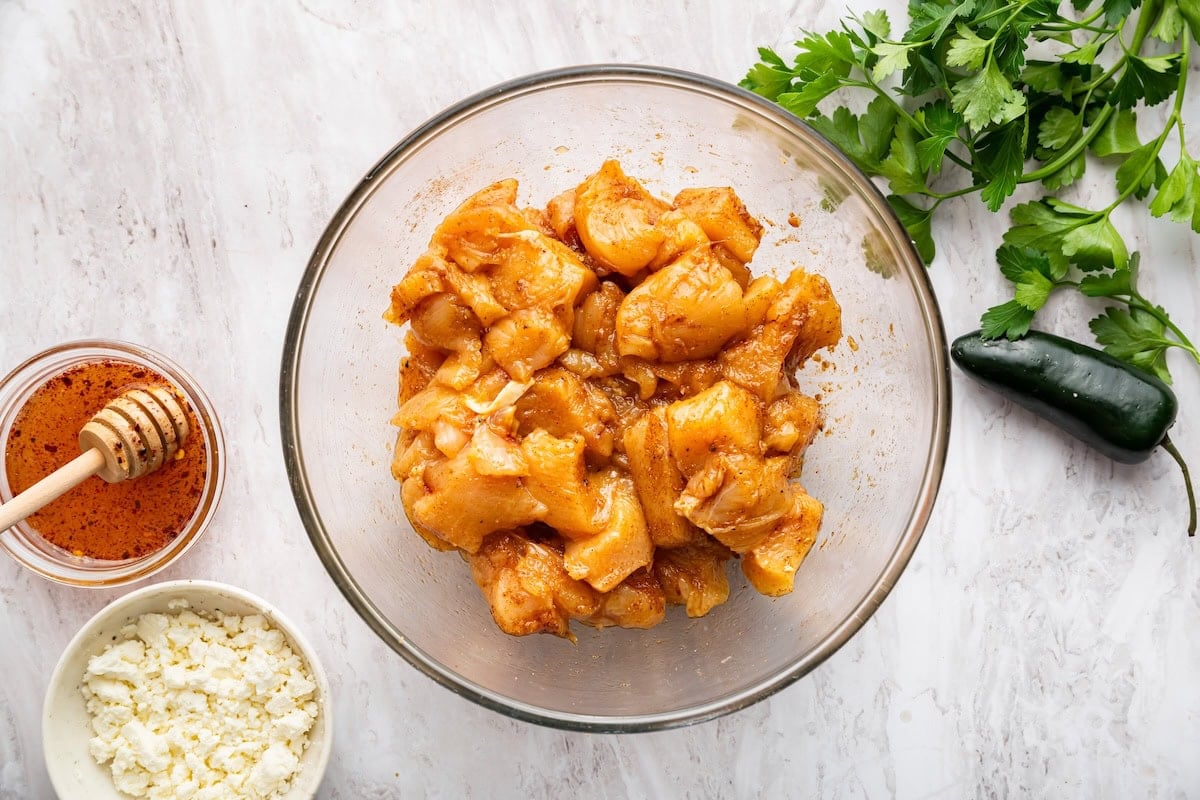 A large glass bowl with seasoned chicken chunks.