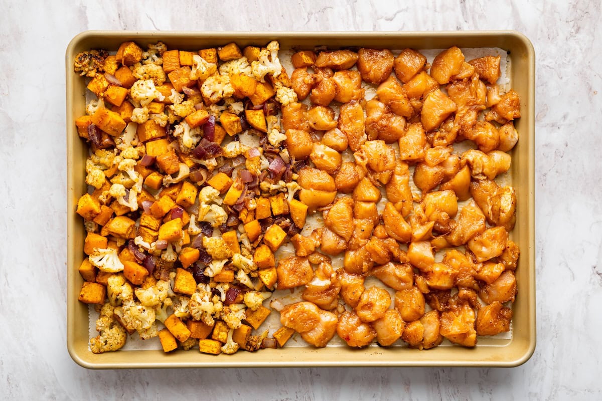A large sheet pan with half of it being roasted veggies and the other half being raw chicken chunks.