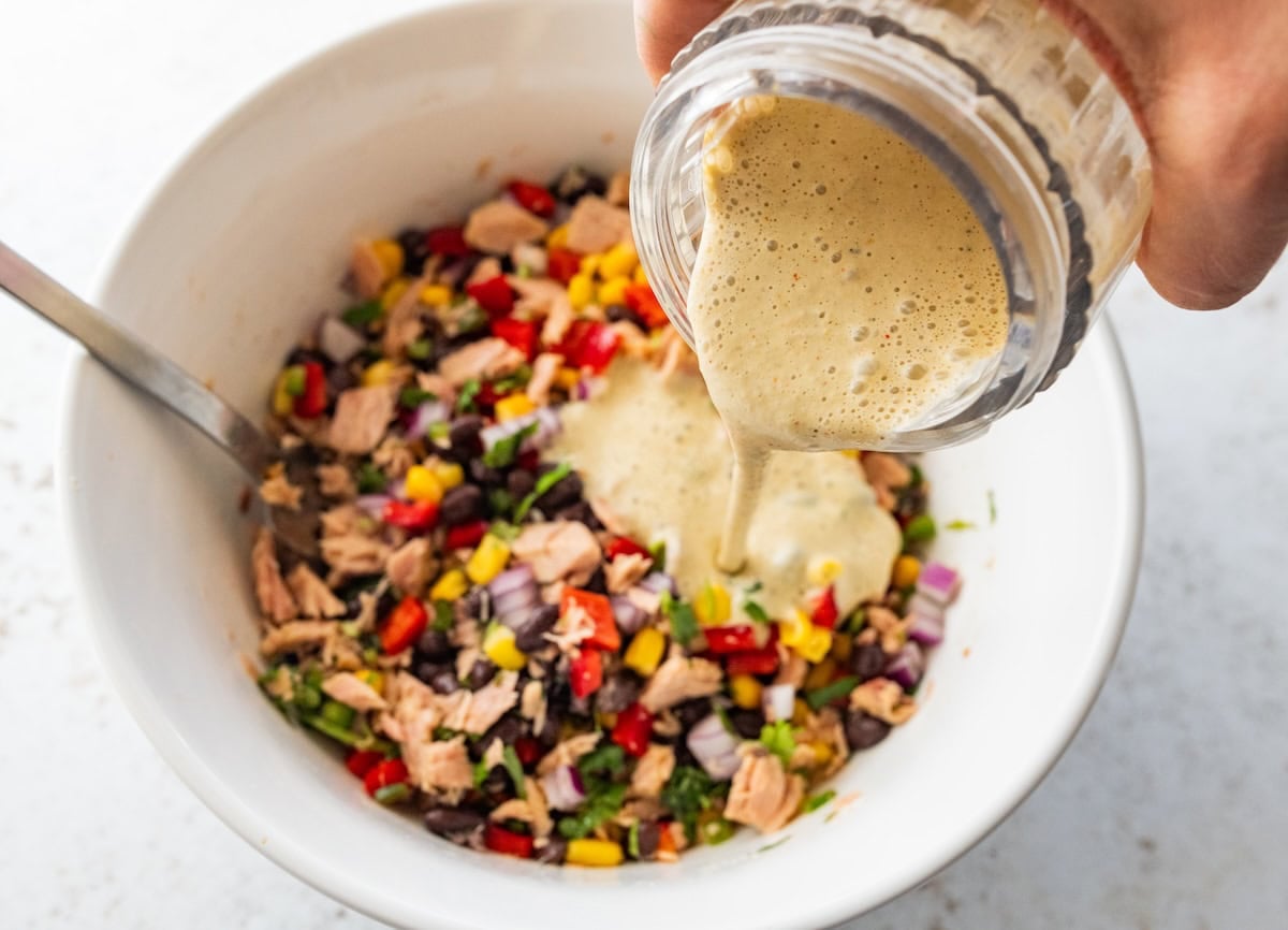 A Greek yogurt sauce is poured in a large bowl with canned tuna, black beans, corn, and vegetables.