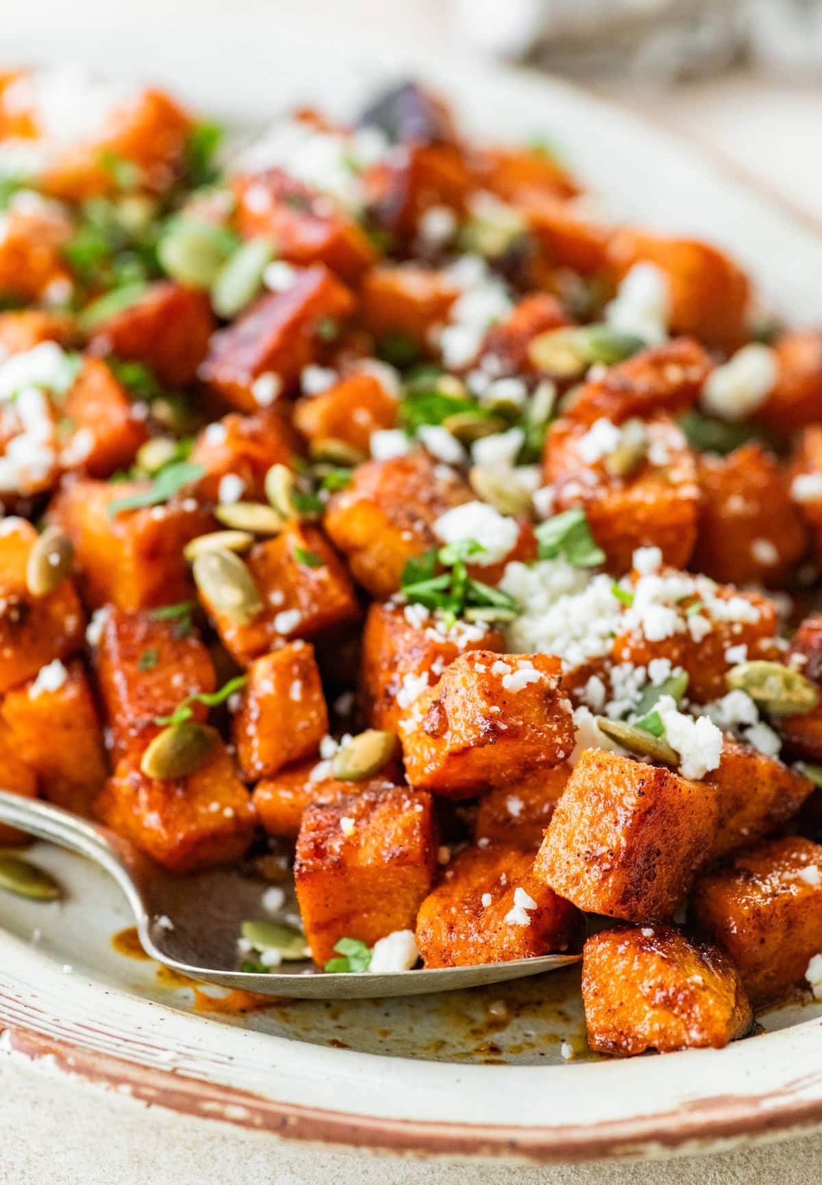 Roasted Mexican sweet potatoes on a large plate topped with cotija, pumpkin seeds, and cilantro.