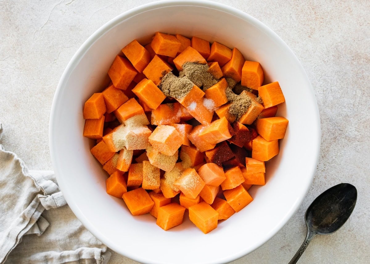 Cubed sweet potatoes in a large mixing bowl with multiple spices.