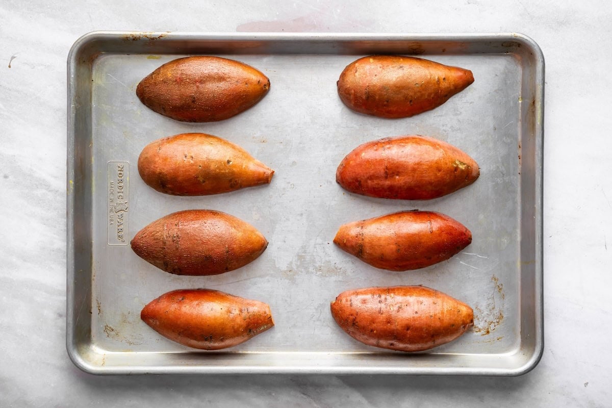 8 sweet potato halves on a baking sheet flesh side down ready to be roasted.