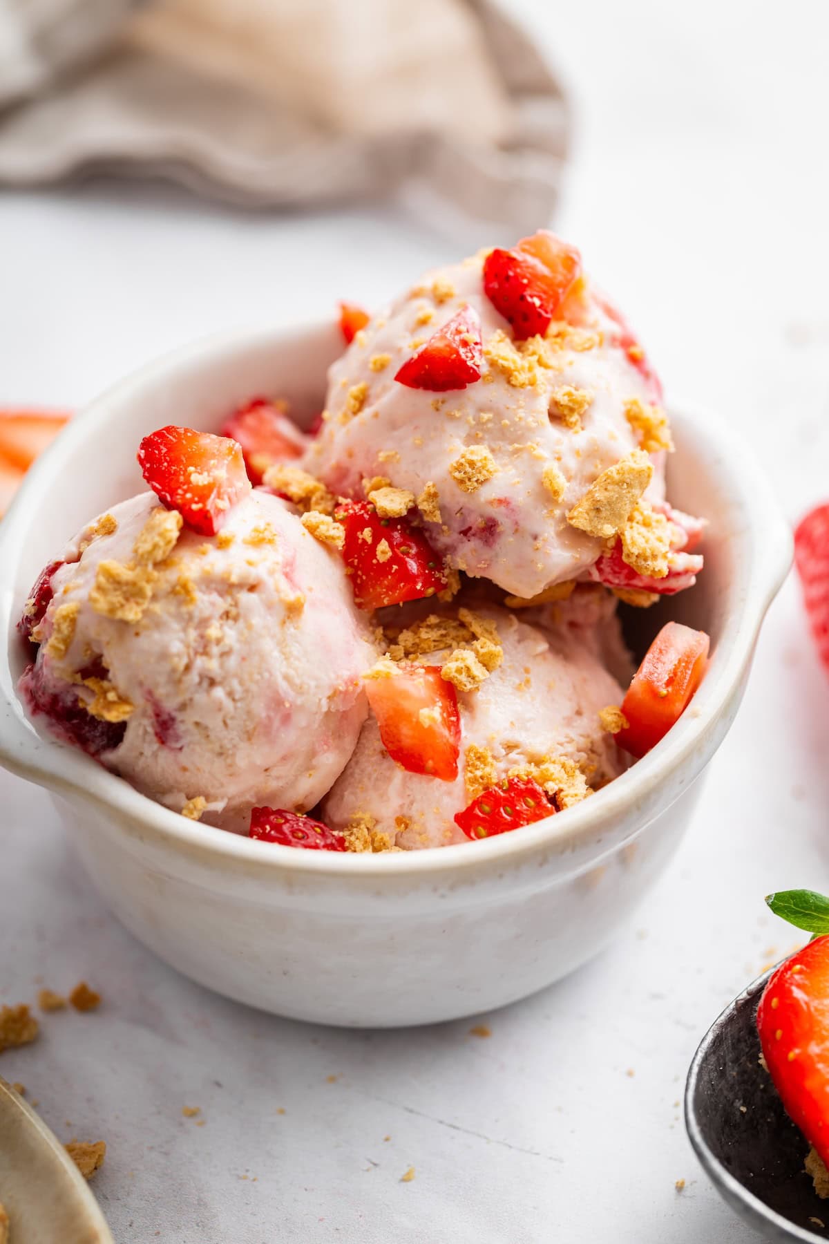 Scoops of strawberry cheesecake cottage cheese ice cream served in a bowl and topped with fresh strawberries and graham crackers.