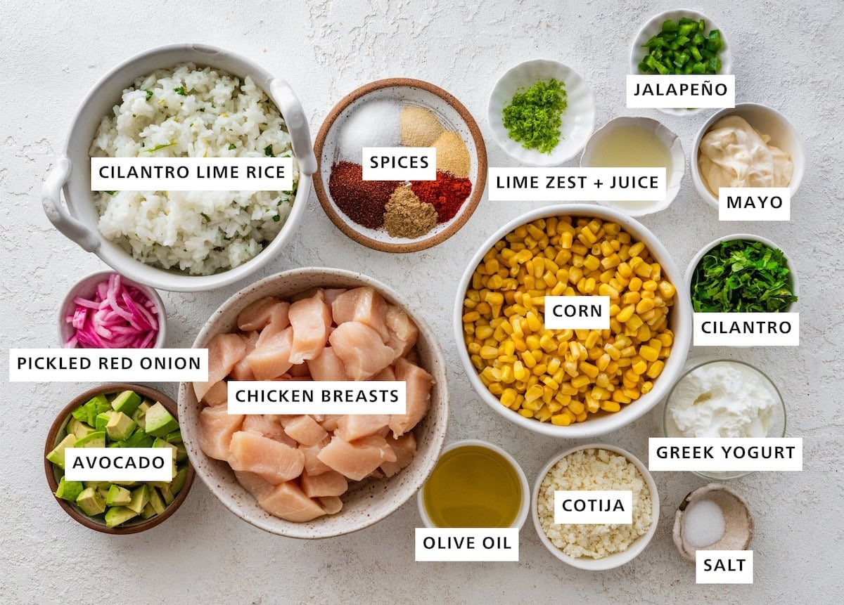 Ingredients measured out for street corn chicken rice bowls: cilantro lime rice, spices, lime zest, lime juice, jalpeno, mayo, cilantro, corn, greek yogurt, salt, cotija, olive oil, chicken breasts, pickled red onion, and avocado.