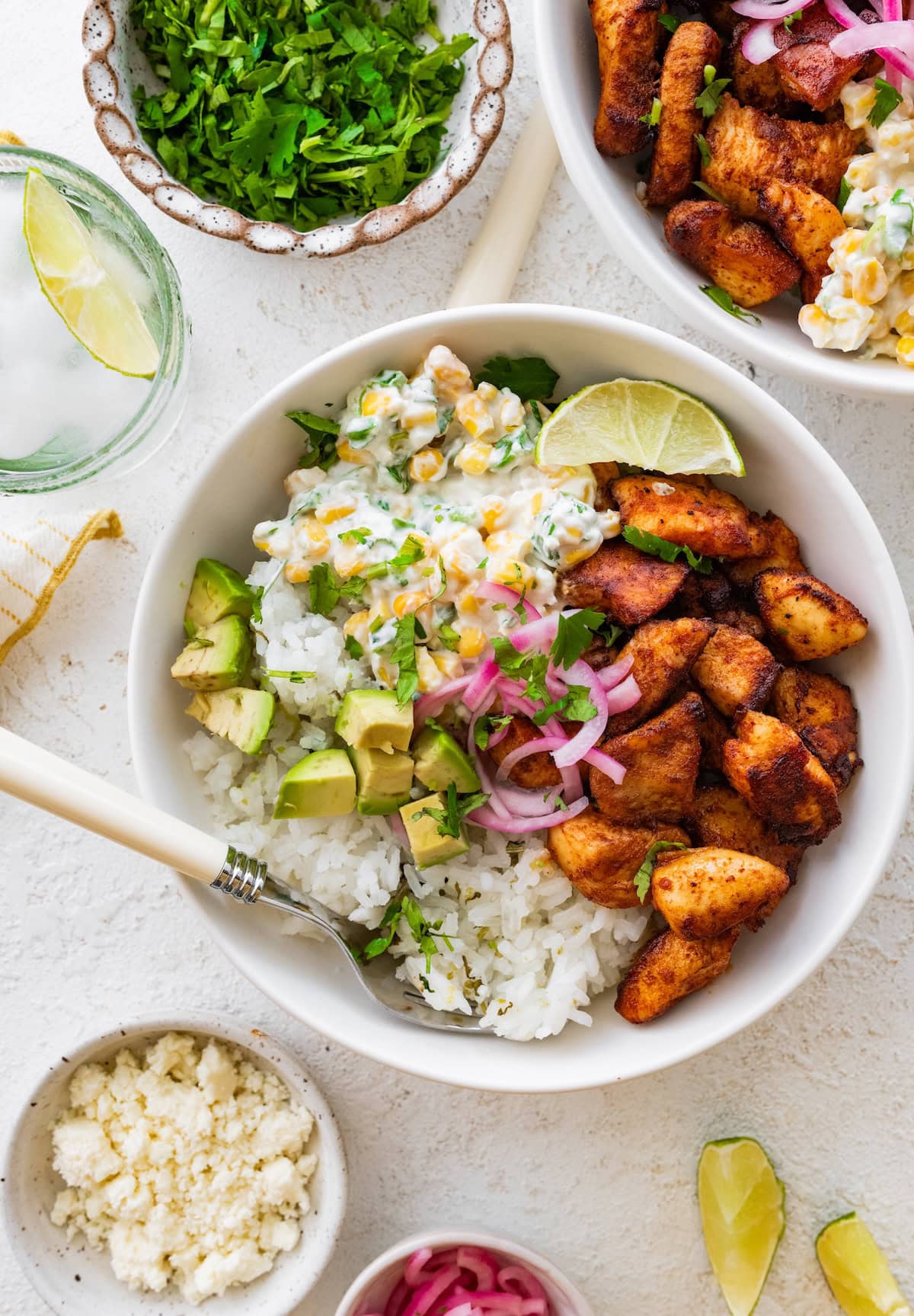 A serving of street corn chicken and rice in a bowl served with avocado, pickled red onion, and a lime wedge.