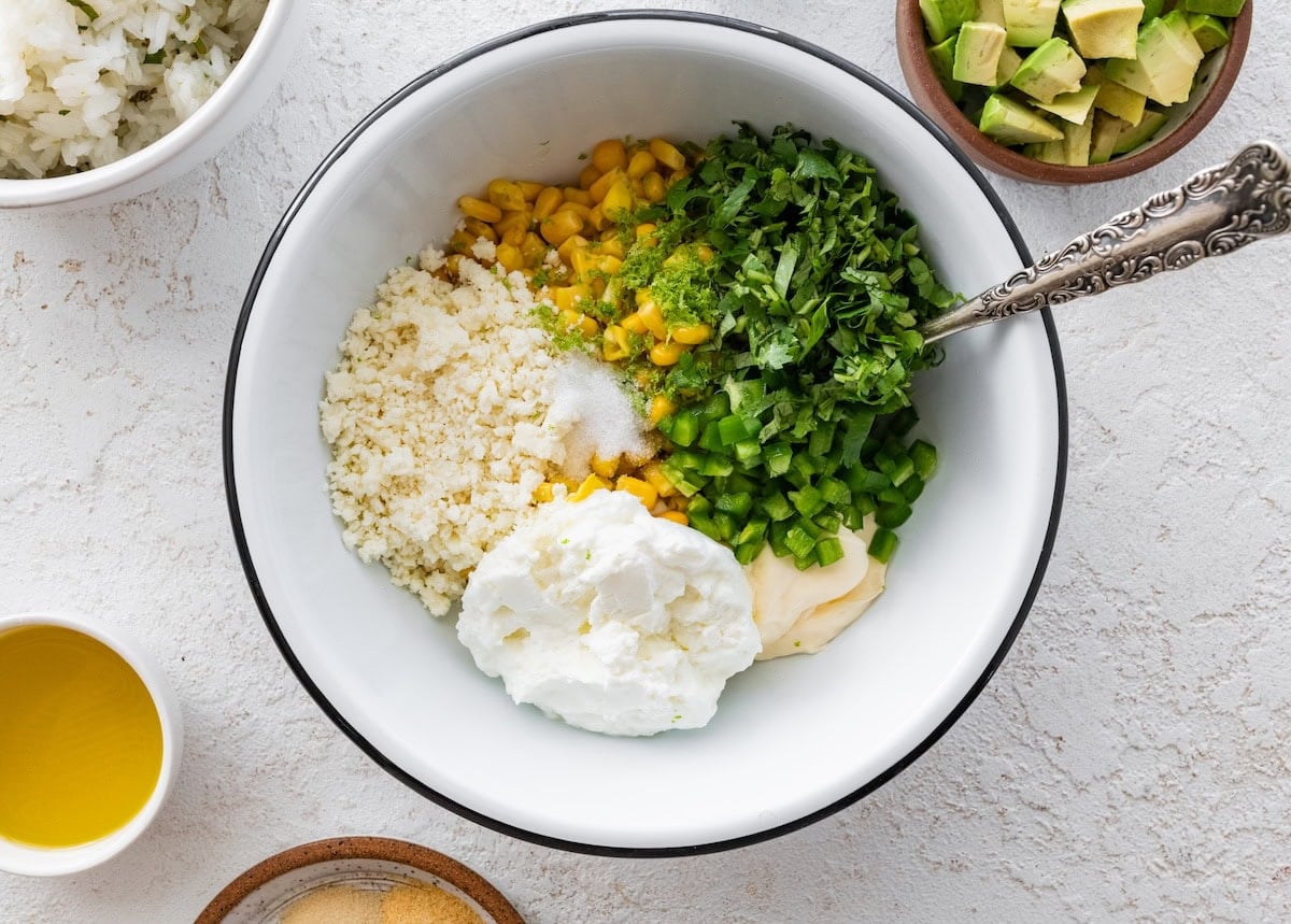 A large mixing bowl with Greek yogurt, mayo, jalapeno, cilantro, corn, and cheese.