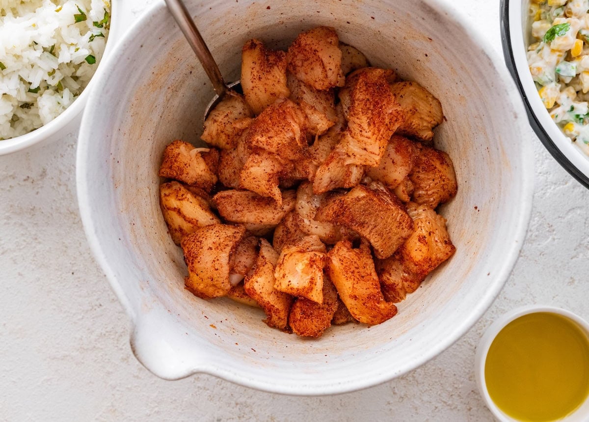 A large mixing bowl with cut up chicken breast. The chicken is raw and seasoned.