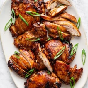 Teriyaki chicken thighs on a large plate topped with fresh green onion.
