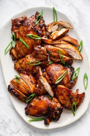 Teriyaki chicken thighs on a large plate topped with fresh green onion.