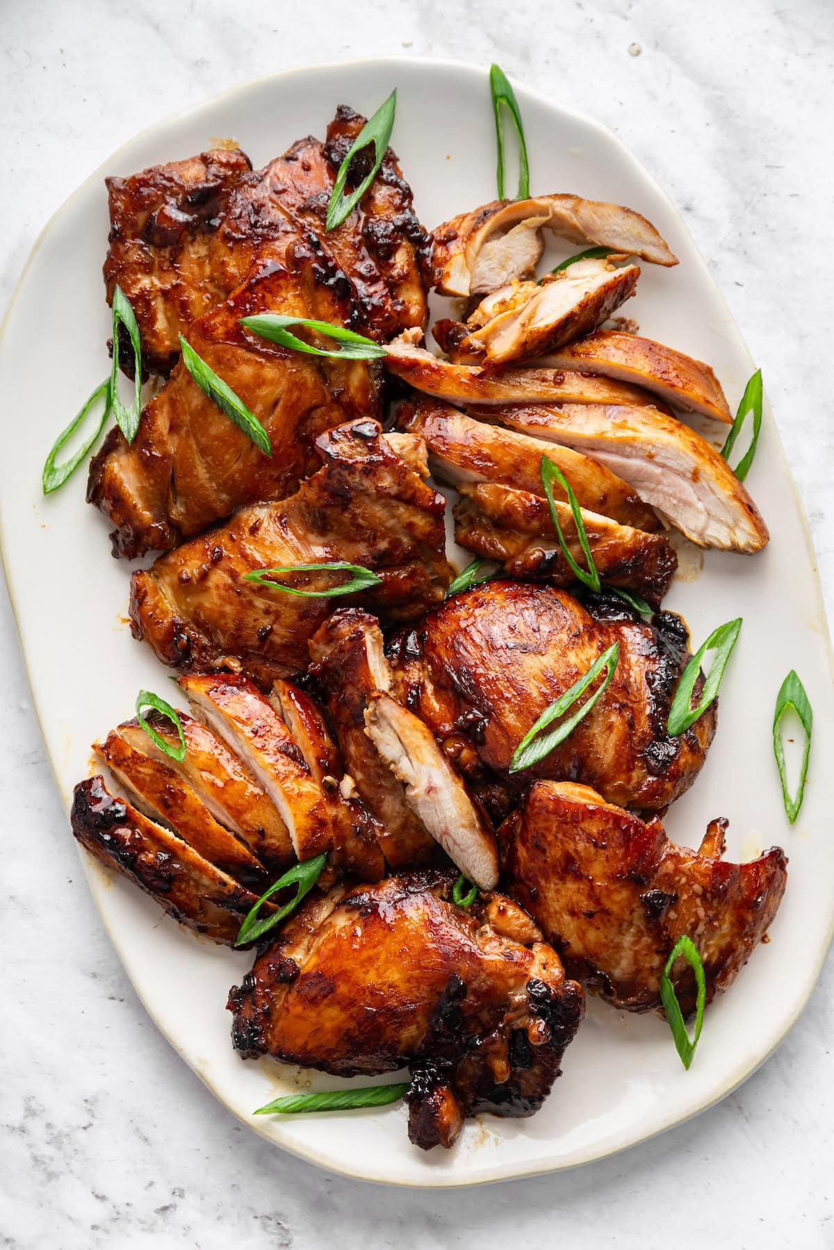 Teriyaki chicken thighs on a large plate topped with fresh green onion.